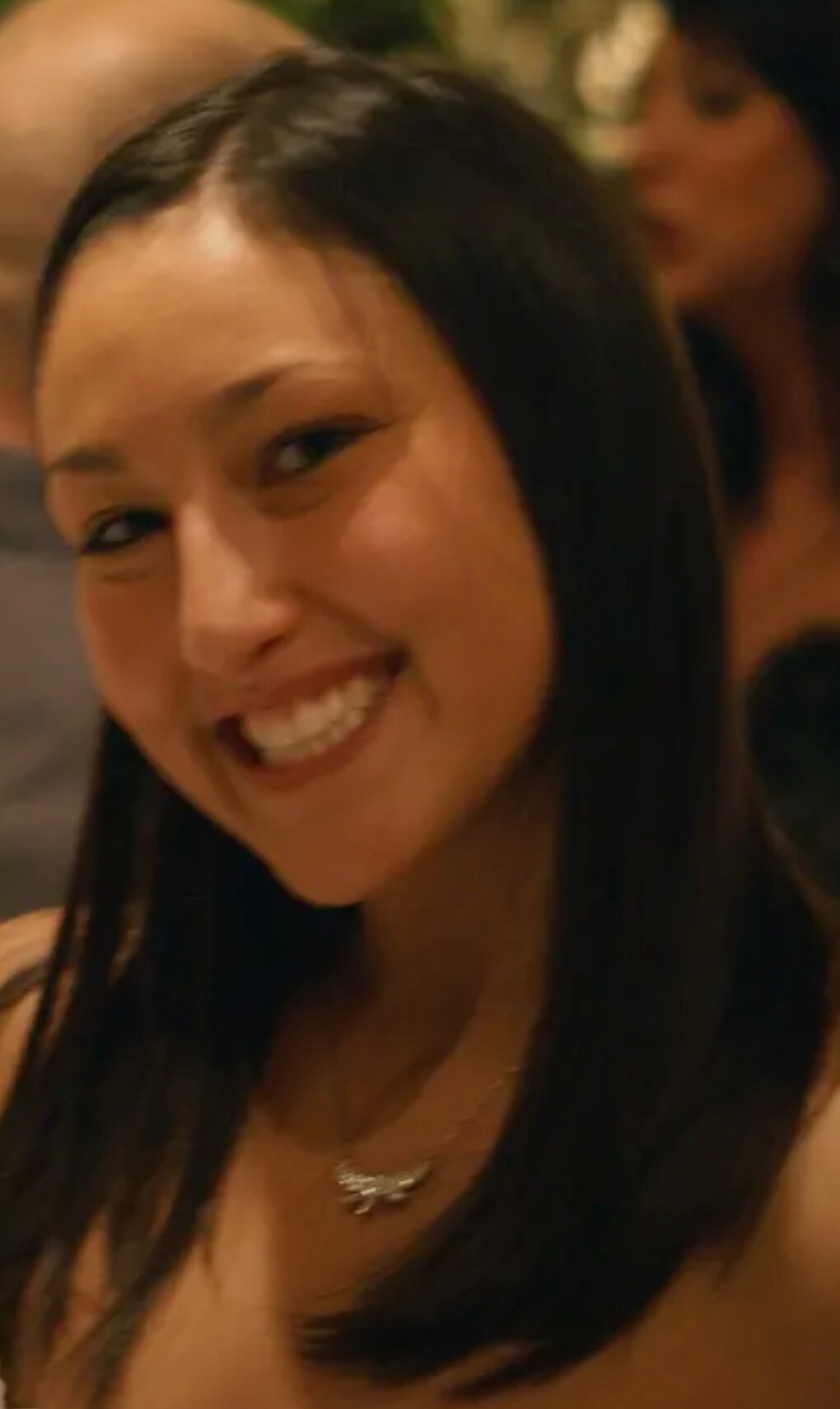Jen laughing at a party, a small silver necklace at her throat, the room blurred behind her.