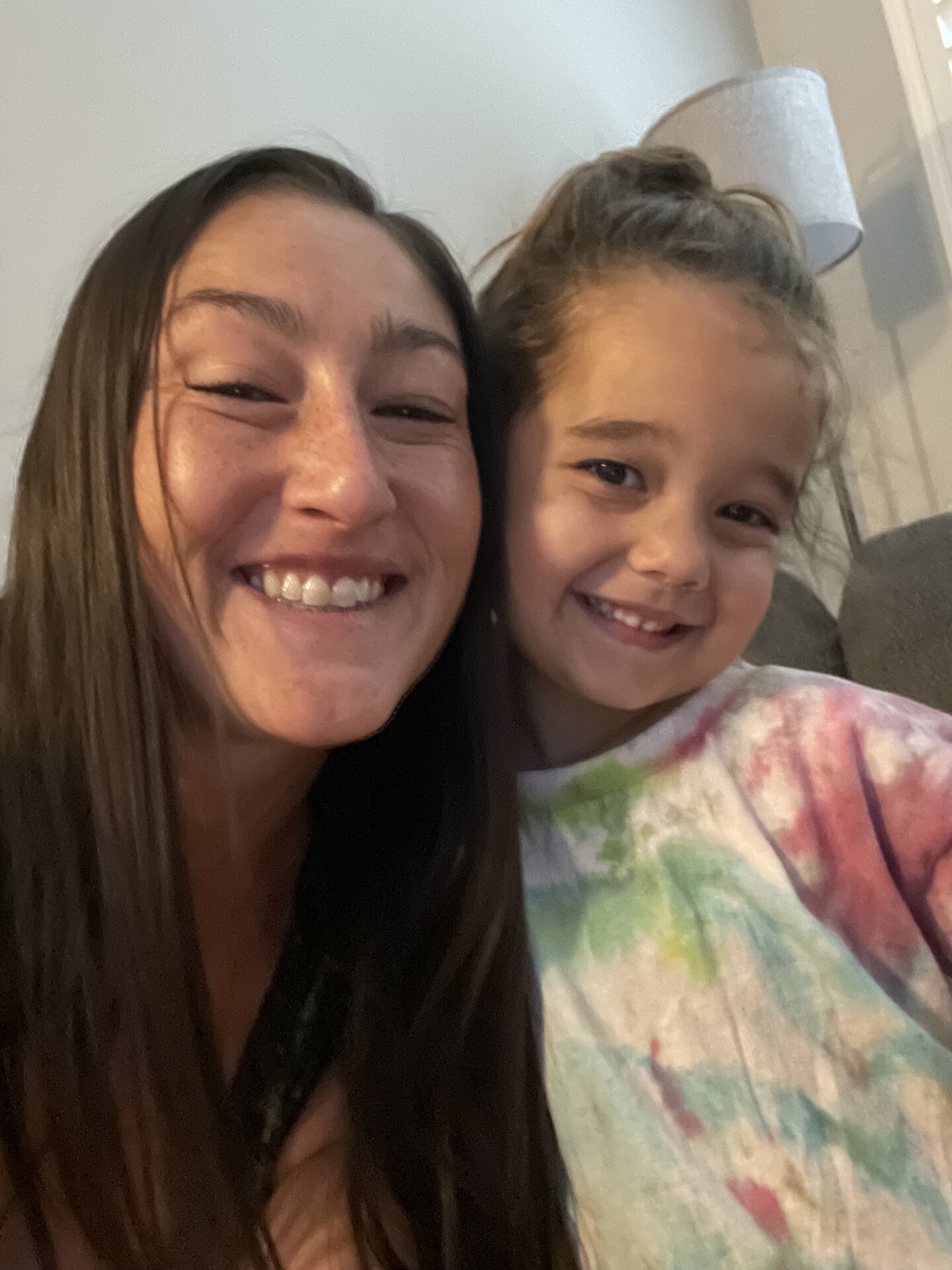 Jen cheek to cheek with a young girl, both grinning at the camera indoors.