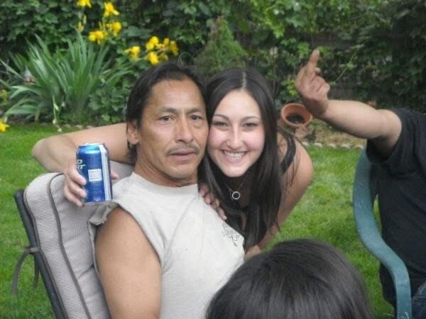 Jen as a teenager, arms wrapped around her dad, the two of them squeezed into one patio chair in a green backyard.